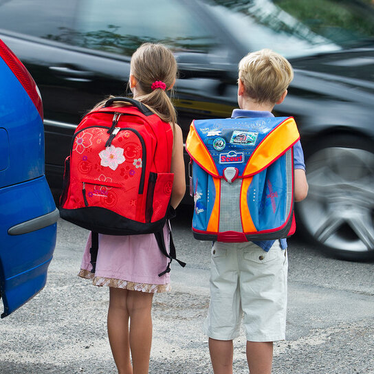 Zwei Schulkinder warten um die Straße zu überqueren