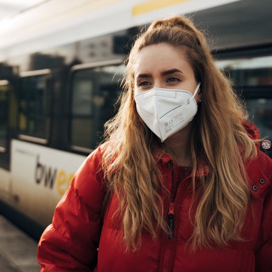 Frau mit FFP2 Maske, mit Zug im Hintergrund