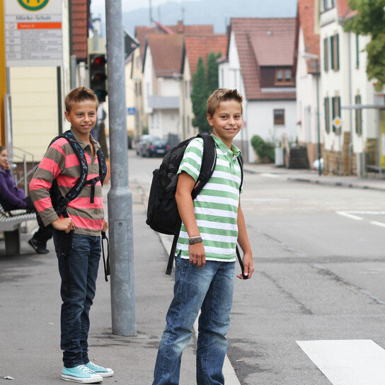 Kinder an Bushaltestelle, vor Zebrastreifen wartend