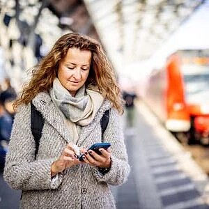 Frau an Bahnsteig mit Handy in der Hand