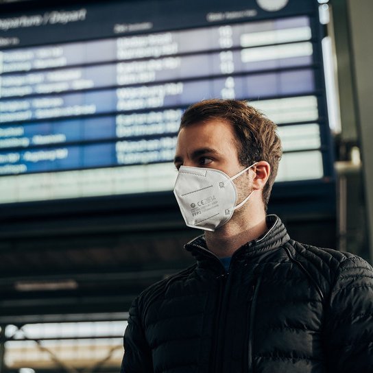 Fahrgast mit FFP-Maske vor Anzeigetafel