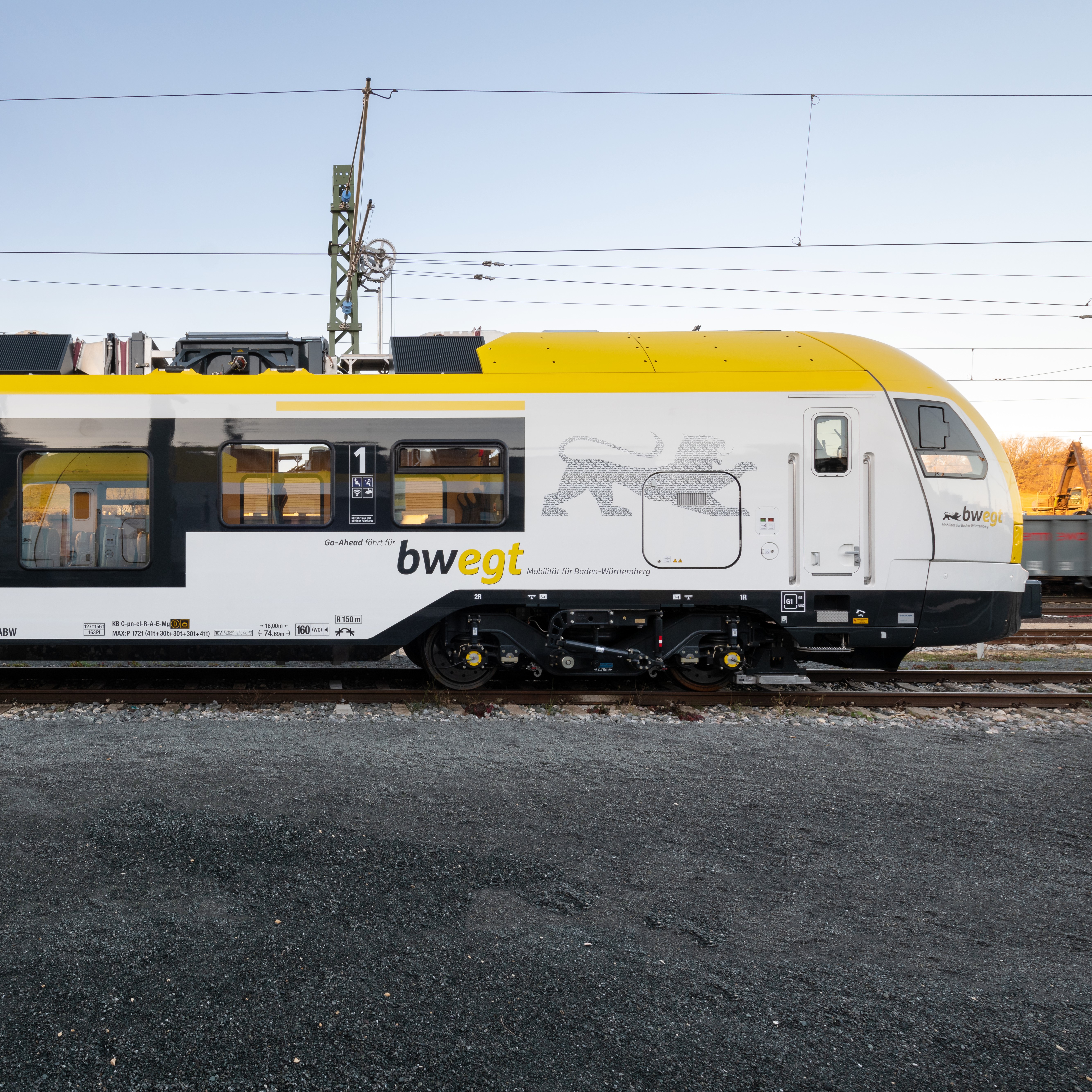 Ein gelb-weißer Zug von bwegt steht auf dem Gleis im Seitenprofil